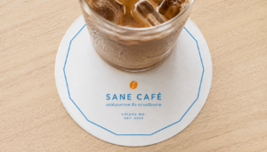 กระดาษรองแก้วพิมพ์โลโก้สีขาวใต้แก้วกาแฟบนโต๊ะร้านกาแฟ